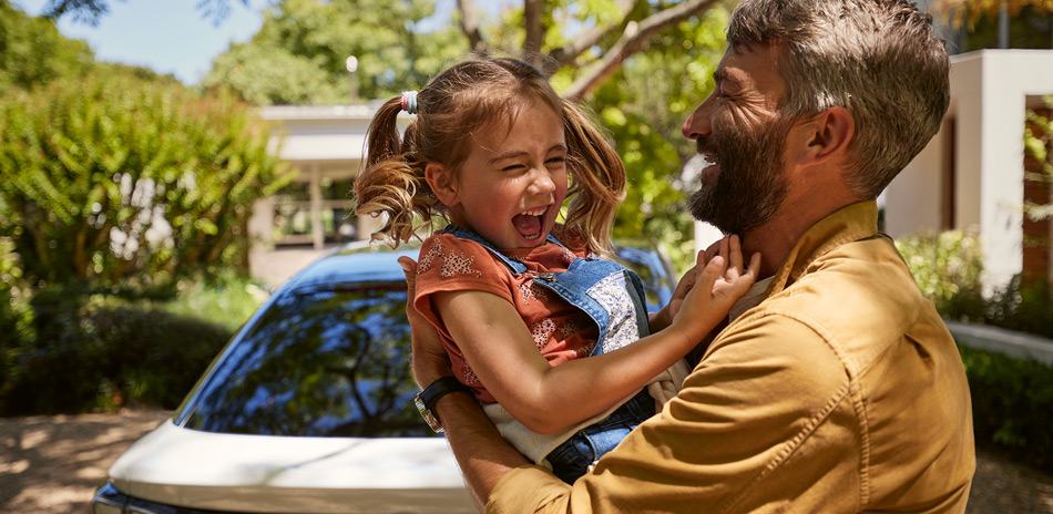 A man holding his laughing daughter infront of a Volkswagen