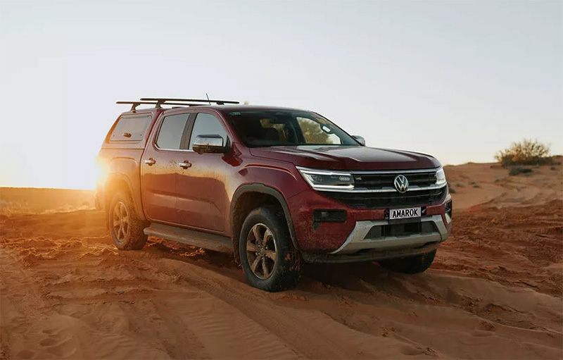 A red ute with a canopy driving on sand