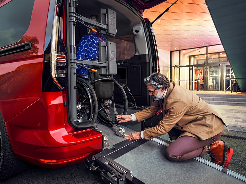 A man securing a wheelchair in the rear of a van