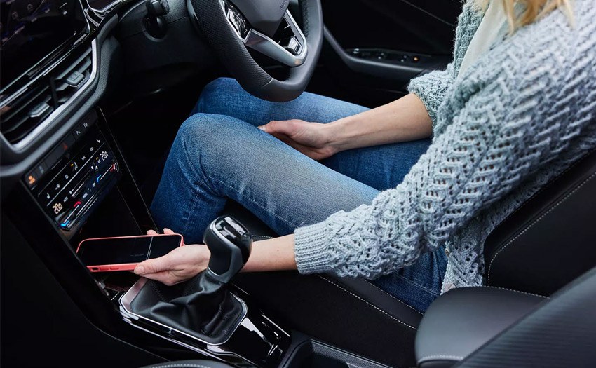 A woman putting a phone in the centre console of an SUV