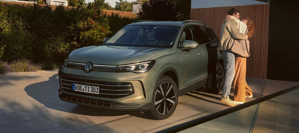 A man cooking a fish on an open fire while sitting in a ute