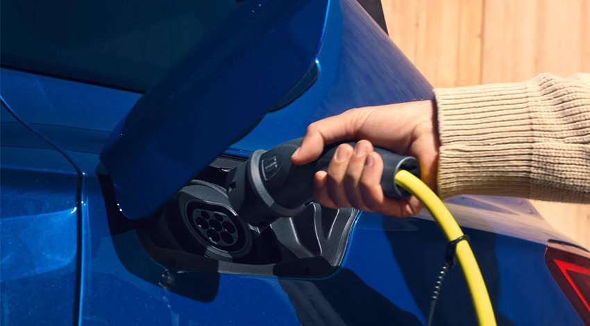 A woman plugging a charger into a blue suv